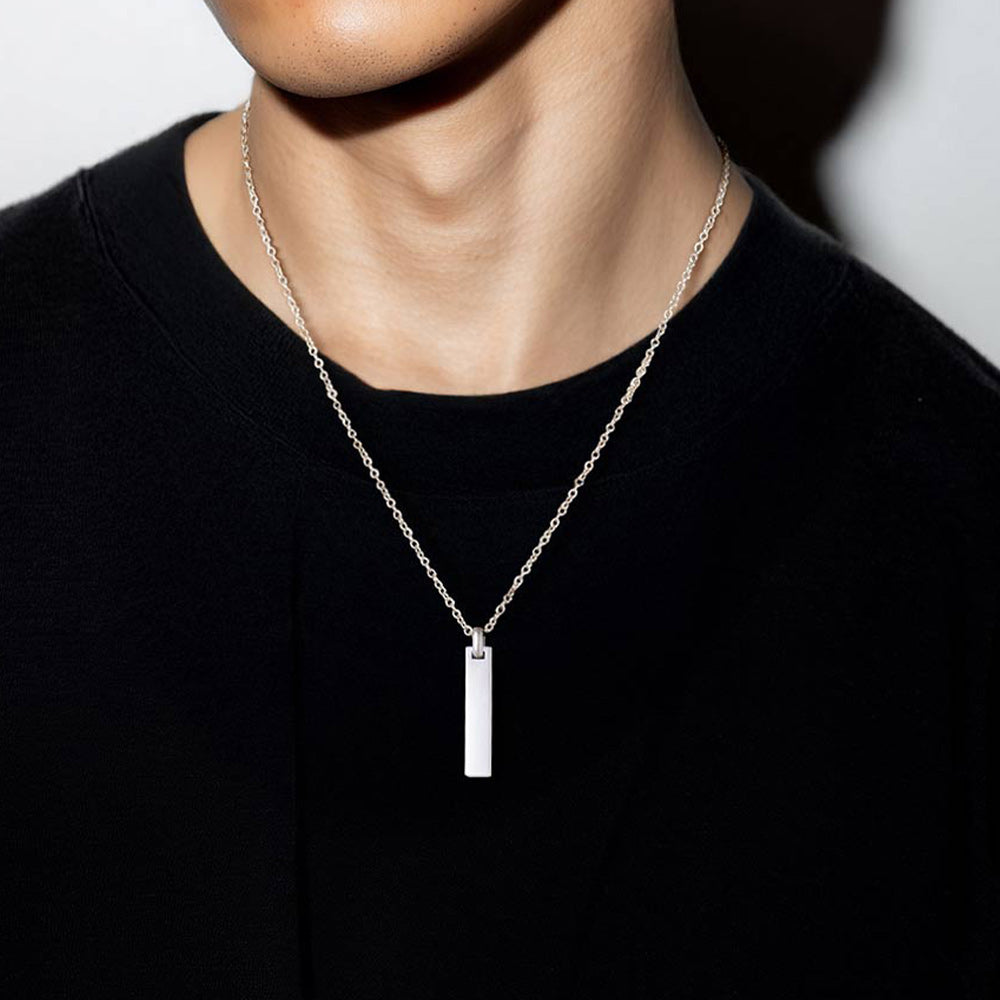 Person wearing a silver bar necklace with a pendant on a plain background