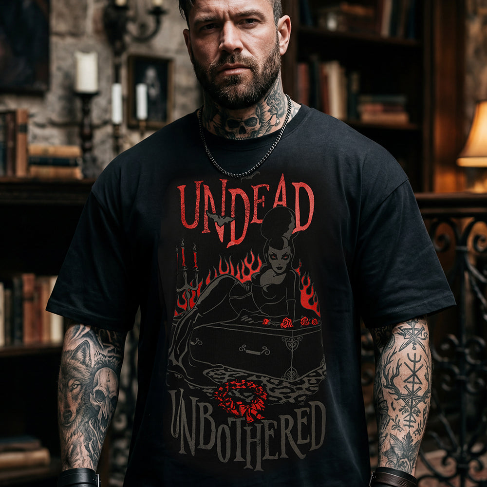 A man with tattoos wearing a black graphic t-shirt with the words 'UNDEAD UNBOOTHERED' and a dark illustration in red and gray, set against a dark, atmospheric background.