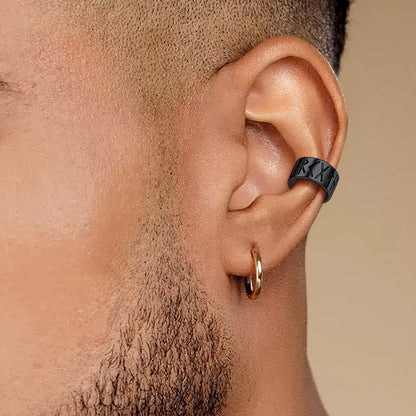 Close-up of a person wearing a black earring cuff and a gold hoop earrings on a beige background