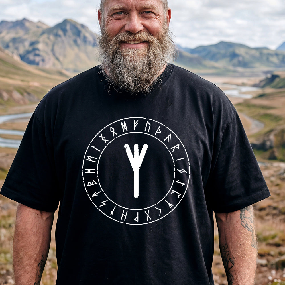 Man wearing a black t-shirt with a white rune symbol and text in a mountainous landscape