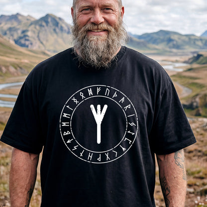 Man wearing a black t-shirt with a white rune symbol and text in a mountainous landscape
