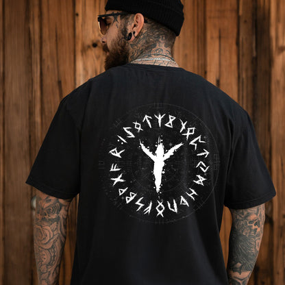 Man wearing a black t-shirt with a white viking rune  design on the back, standing against a wooden wall.