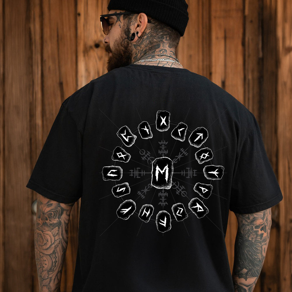 Person wearing a black t-shirt with a viking rune design on the back, standing against a wooden wall.
