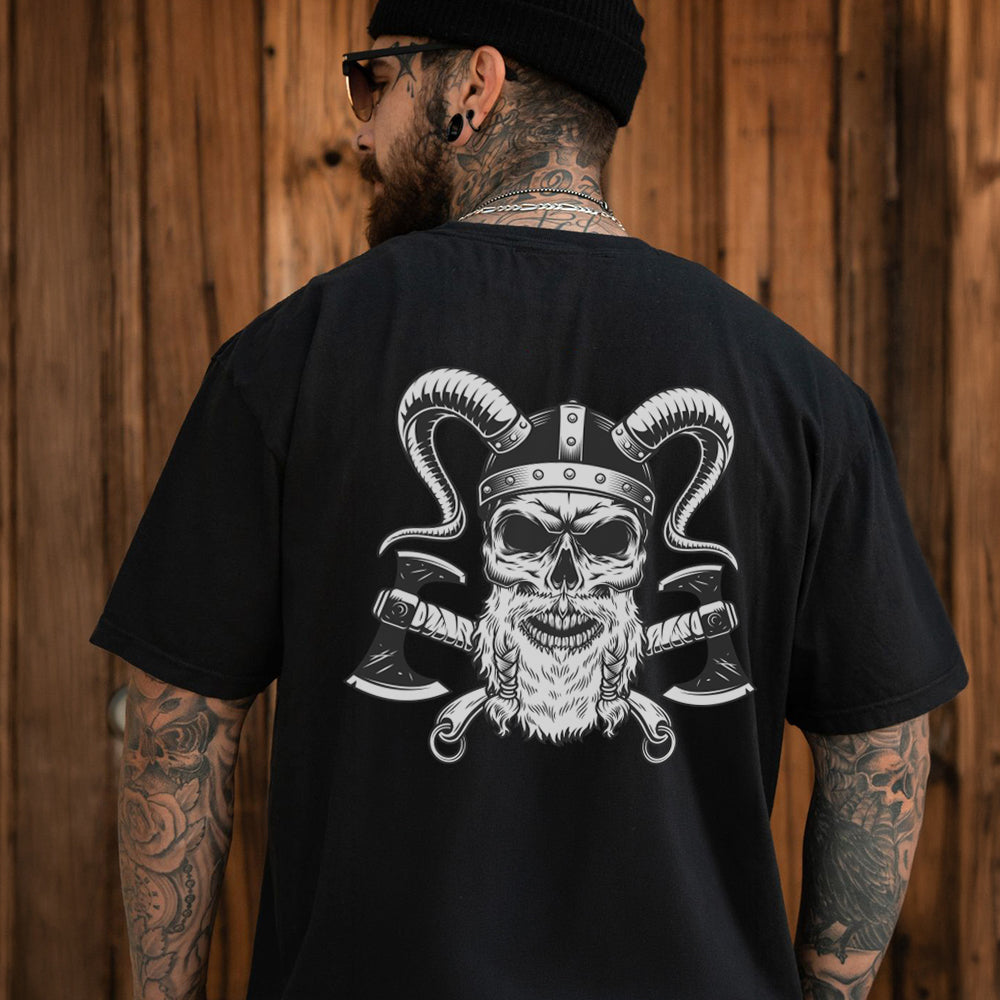 Man wearing a black t-shirt with a skull and crossed axes design on the back, standing against a wooden wall.