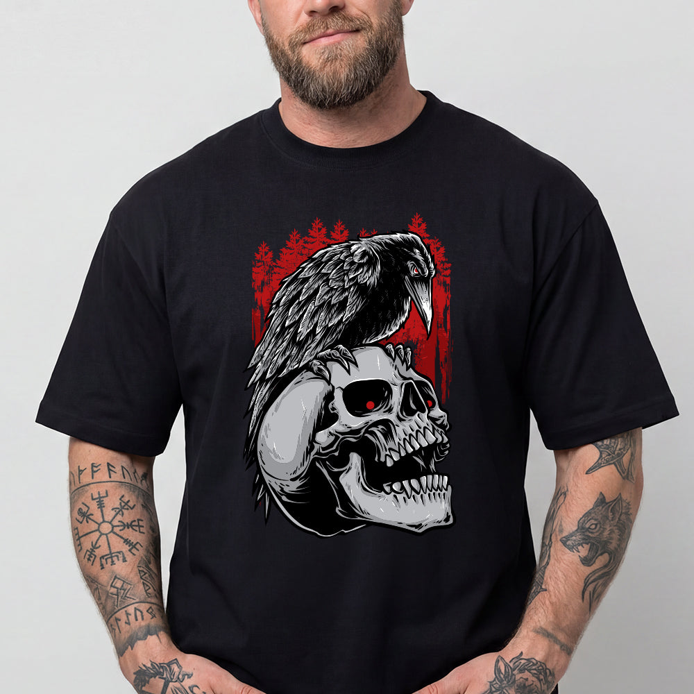 A man wearing a black short-sleeve t-shirt with a graphic print of a raven perched on a skull, set against a red forest background. 