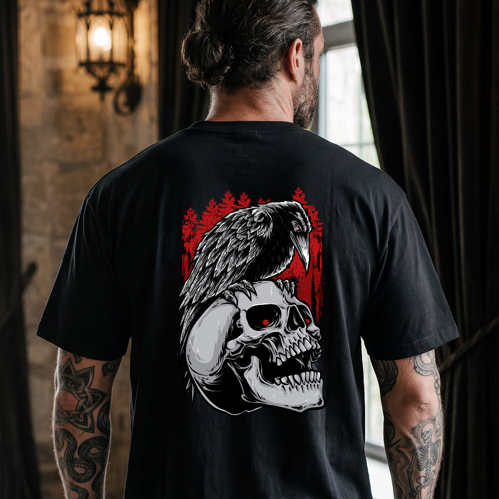 A man viewed from behind wearing a black t-shirt with a large graphic print on the back featuring a raven perched on a skull with red eyes, set against a dark red forest background.