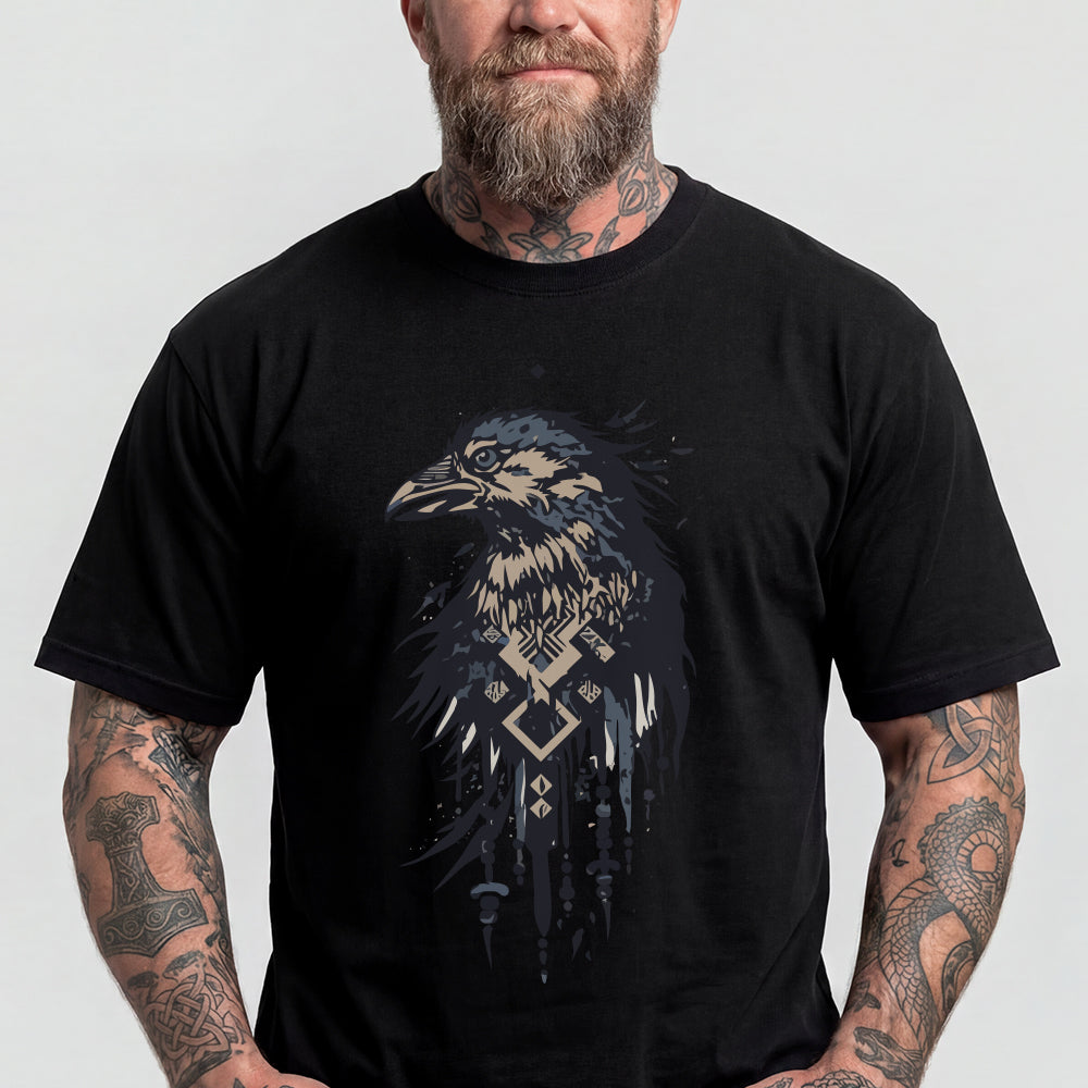 A man wearing a black short-sleeve t-shirt with a detailed graphic of a raven in shades of blue, beige, and white, featuring geometric patterns.