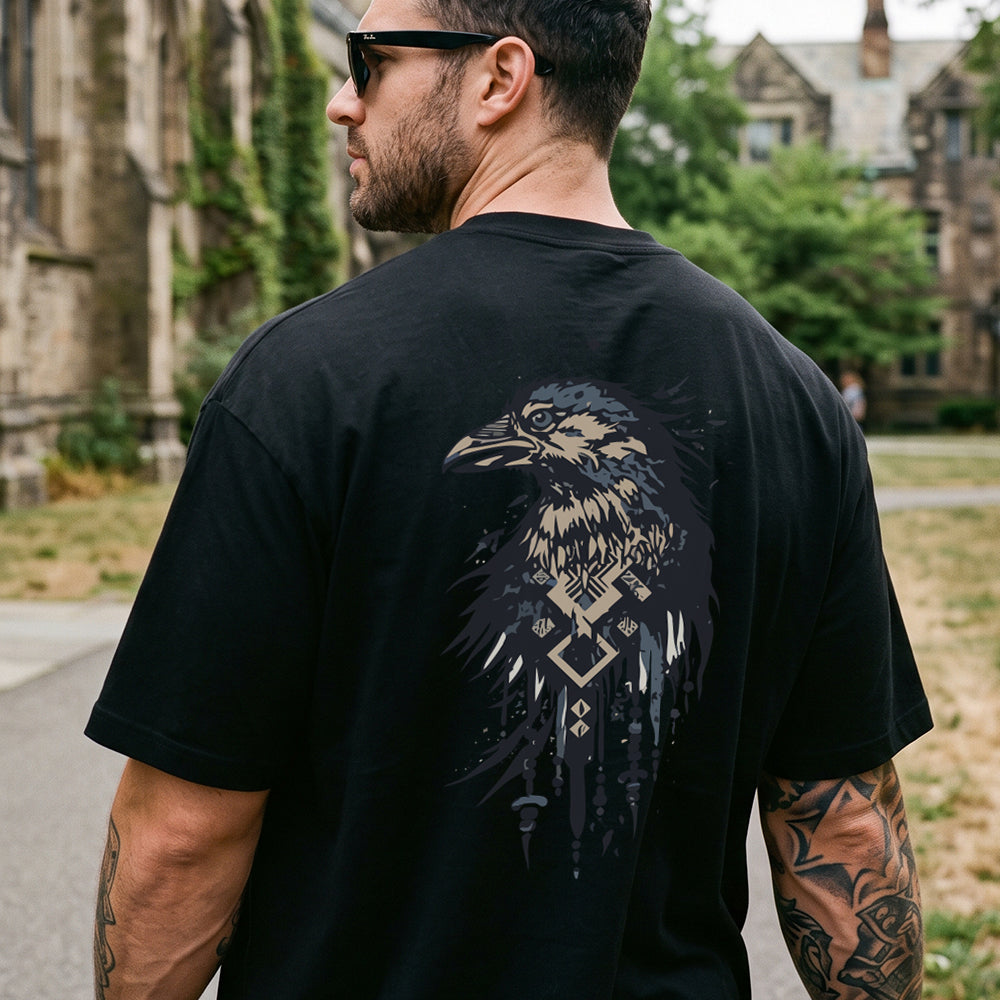 A man wearing a black t-shirt with a large raven graphic on the back, photographed from behind in an outdoor campus setting.