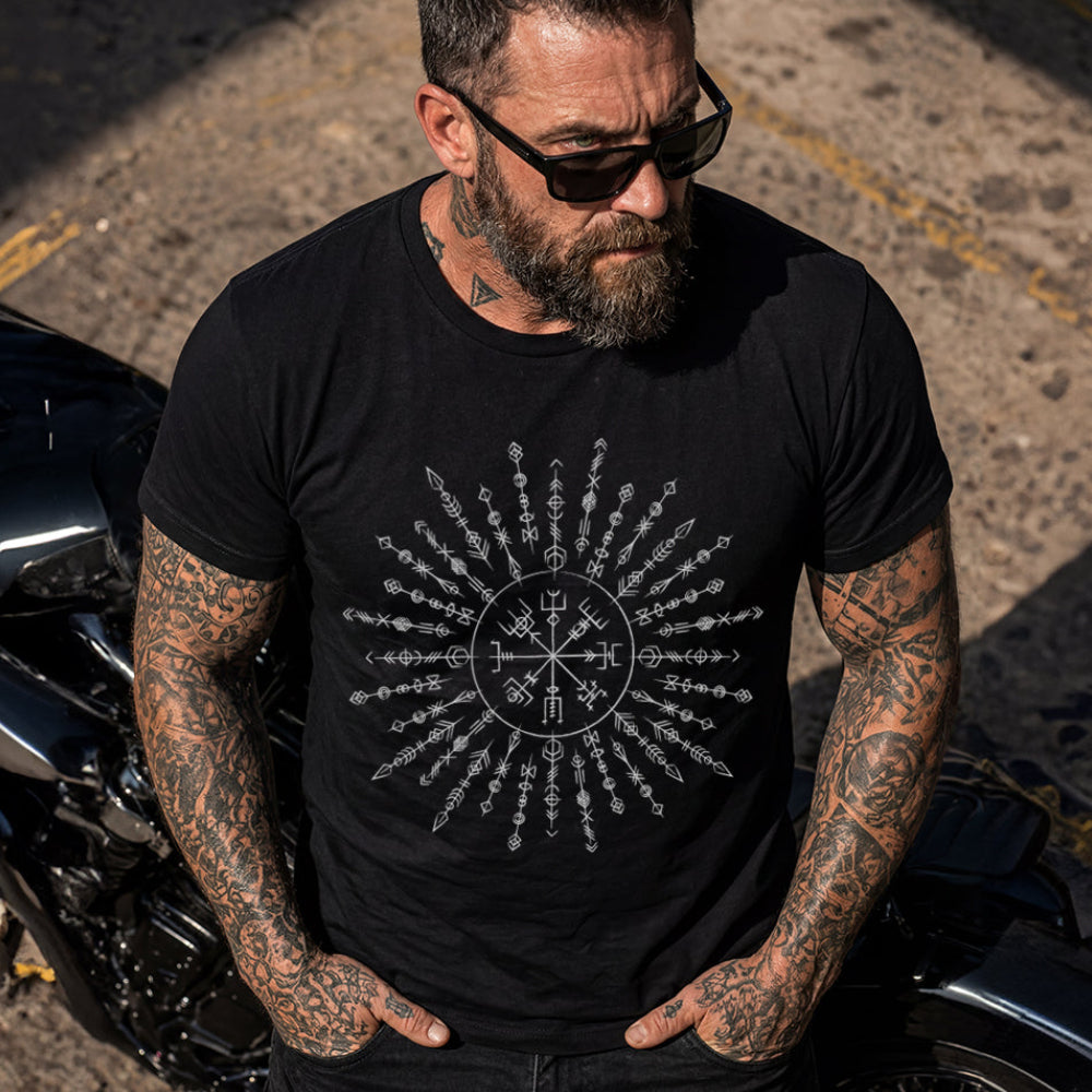 Man wearing a black t-shirt with a Viking Rune design, standing next to a motorcycle.