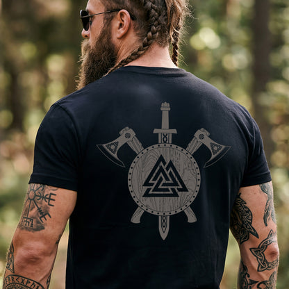 Man wearing a black Viking Valknut Shield Sword & Axes T-Shirt on the back, standing in a forest.