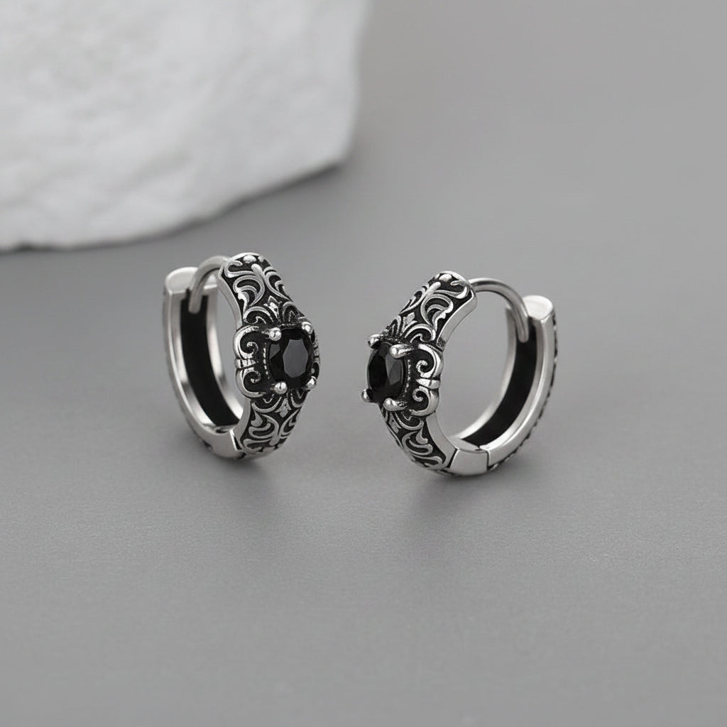 Silver hoop earrings with black gemstones on a gray surface
