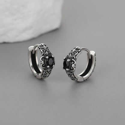 Silver hoop earrings with black gemstones on a gray surface