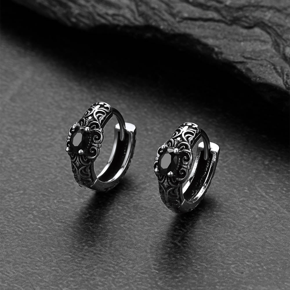 Pair of silver hoop earrings with intricate designs on a dark textured surface