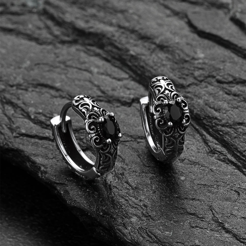Pair of silver hoop earrings with intricate designs on a dark stone surface