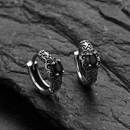 Pair of silver hoop earrings with intricate designs on a dark stone surface