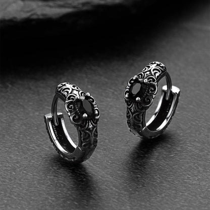 Pair of silver hoop earrings with intricate designs on a dark surface