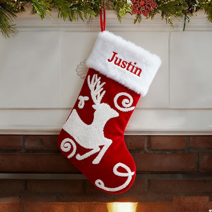 Red Christmas stocking with white reindeer design and 'Justin' embroidery, hanging on a fireplace.